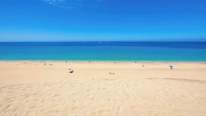 Une vaste plage de sable fin, avec une eau d’un bleu limpide et quelques bateaux qui se dessinent à l’horizon.