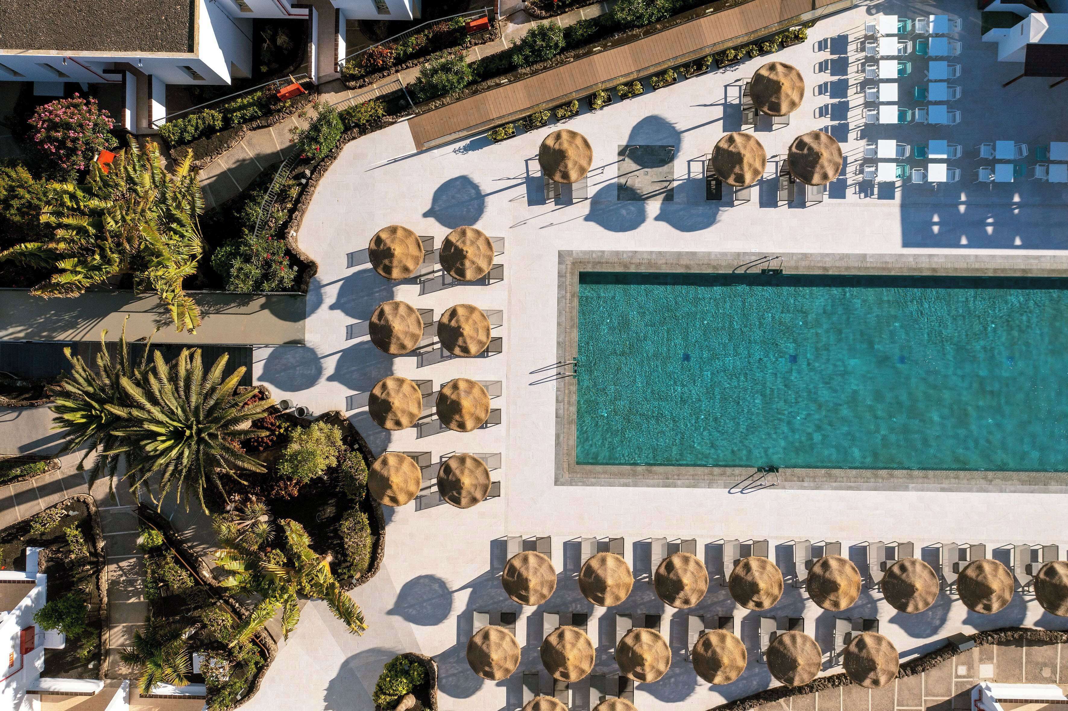 An aerial view of a resort with a large pool, sun loungers, and palm trees.