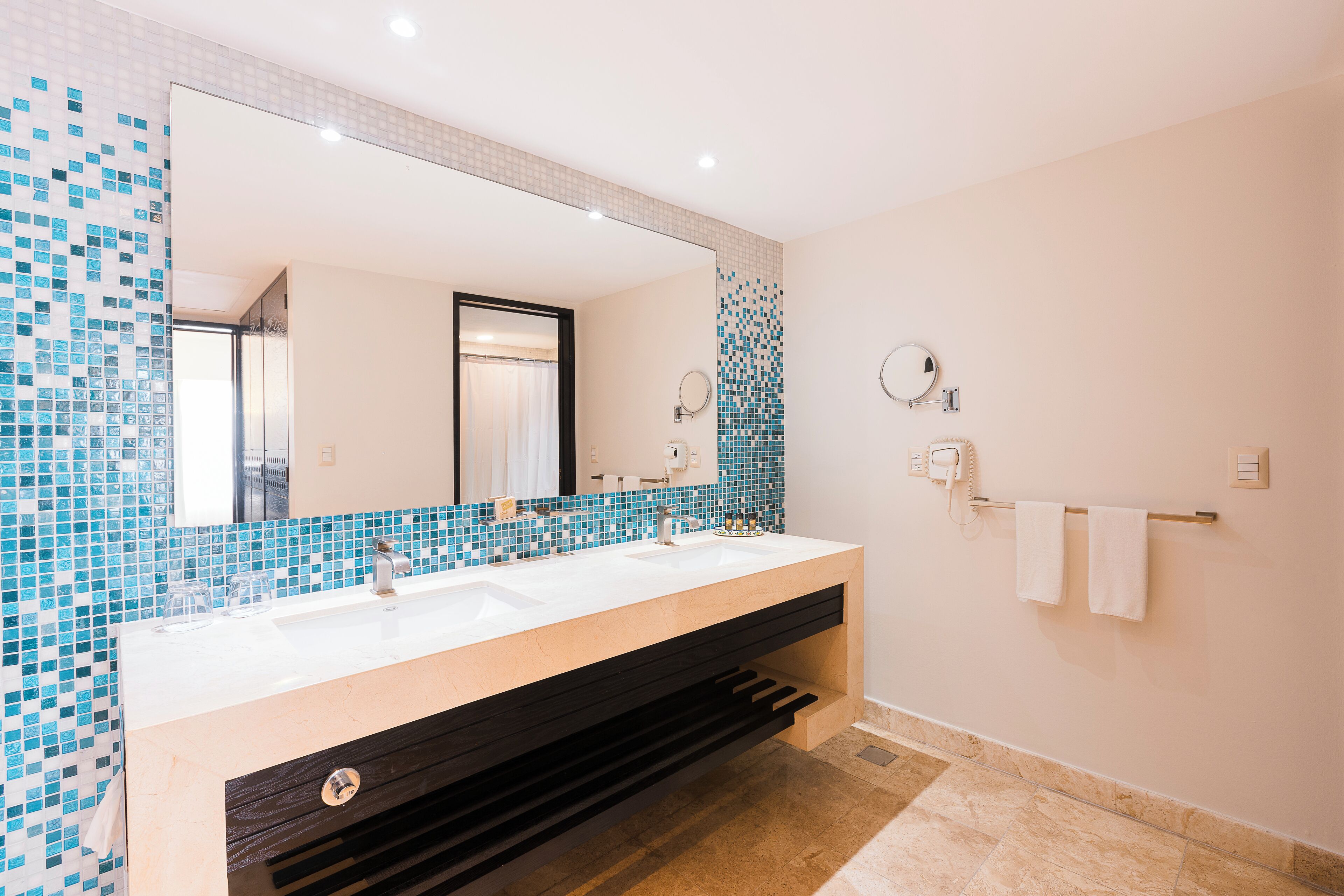 Un baño moderno con un espejo grande, dos lavamanos y un perchero para toallas.