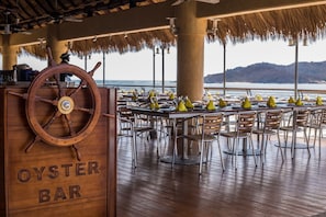 A wooden bar with a ship's wheel, tables with yellow umbrellas, and a view of the sea.