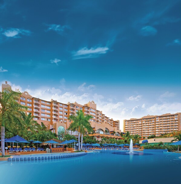 A hotel with multiple balconies, a swimming pool, and palm trees.