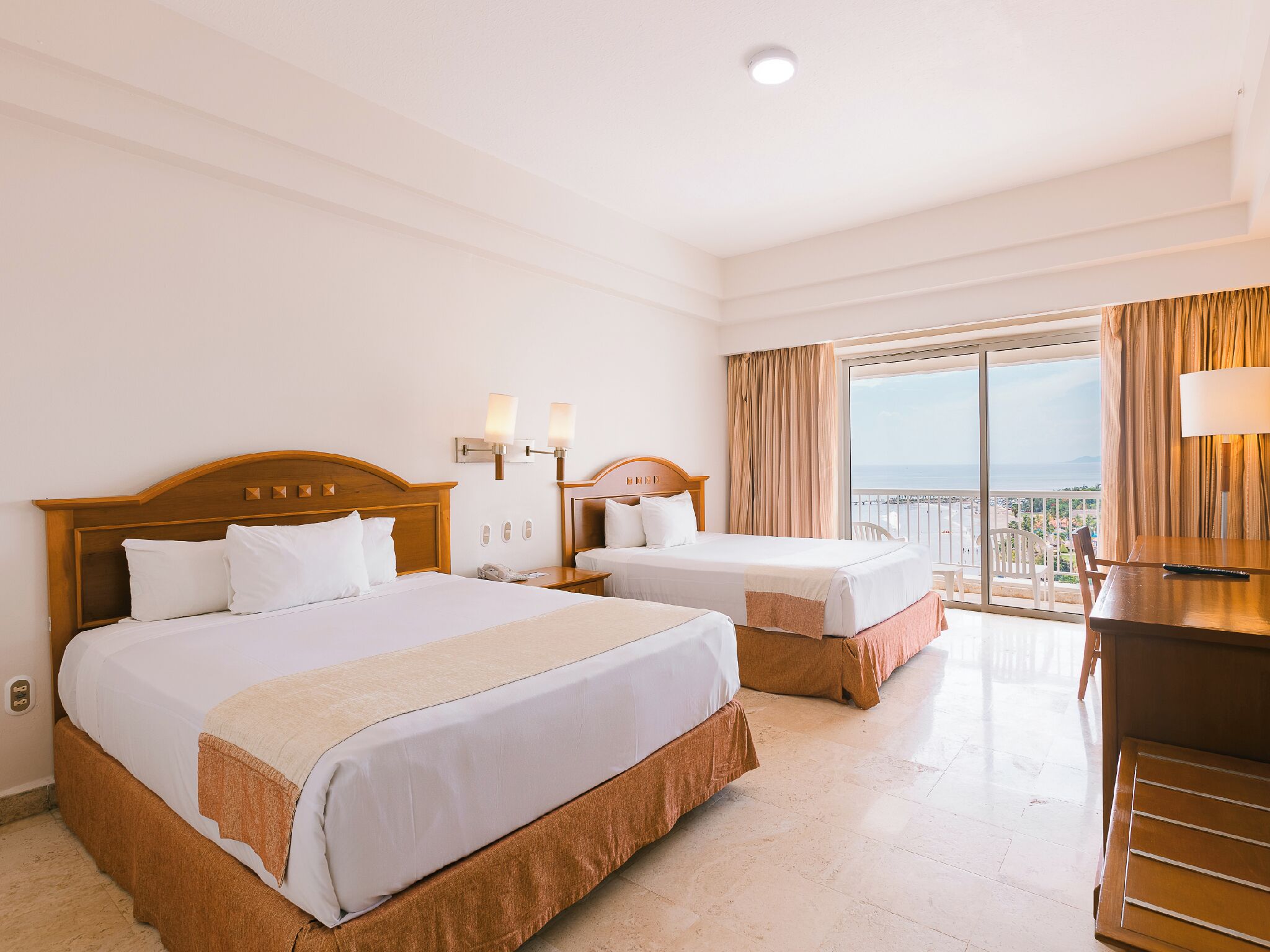 Habitación de hotel con dos camas, un escritorio y un balcón con vistas.