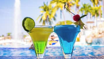 Two cocktails in glasses with a pool and palm trees in the background.