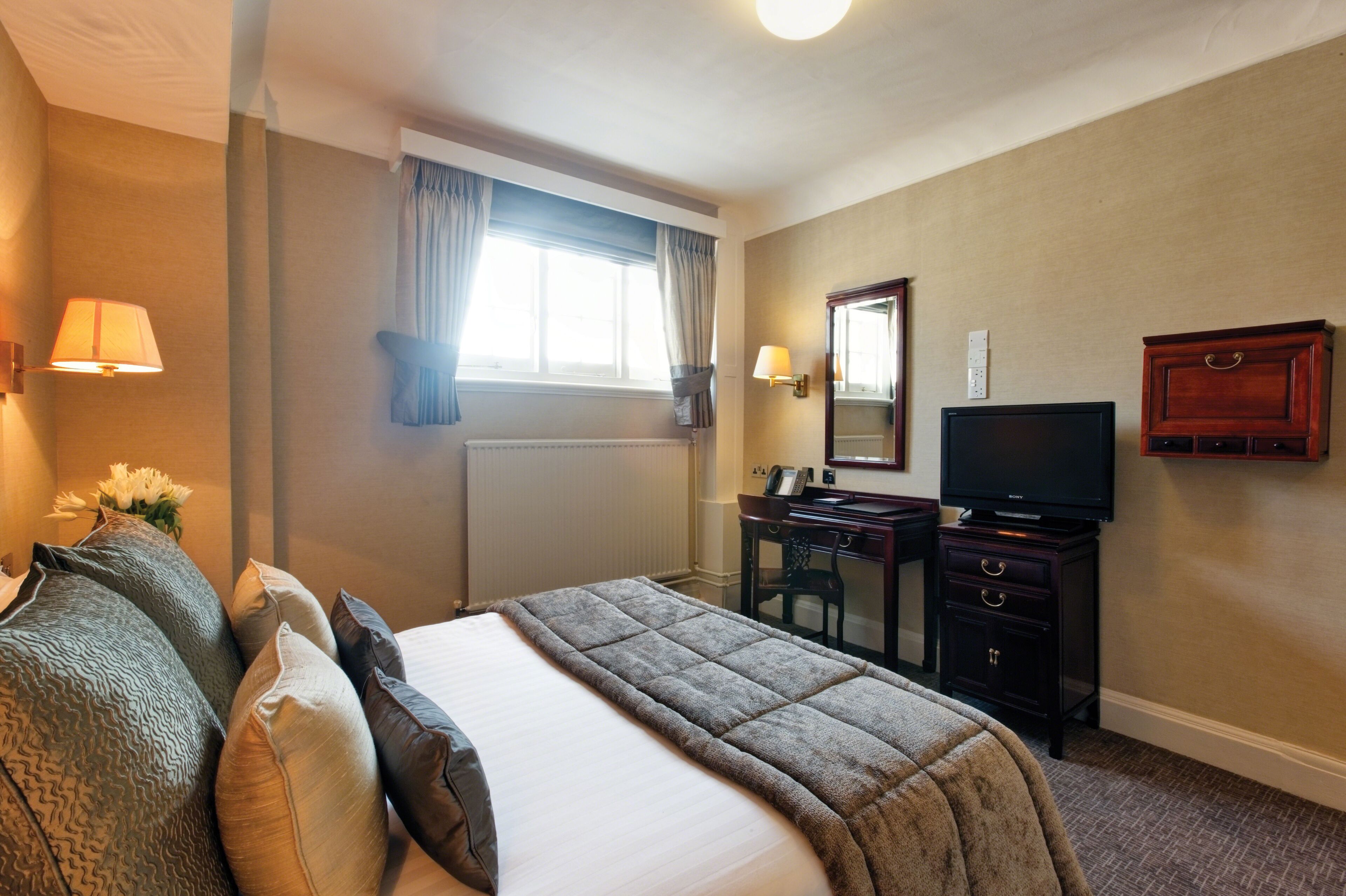 Una habitación de hotel con cama, escritorio, televisión y cómoda.