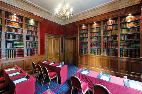 A library with rows of bookshelves, tables with red tablecloths, and chairs.