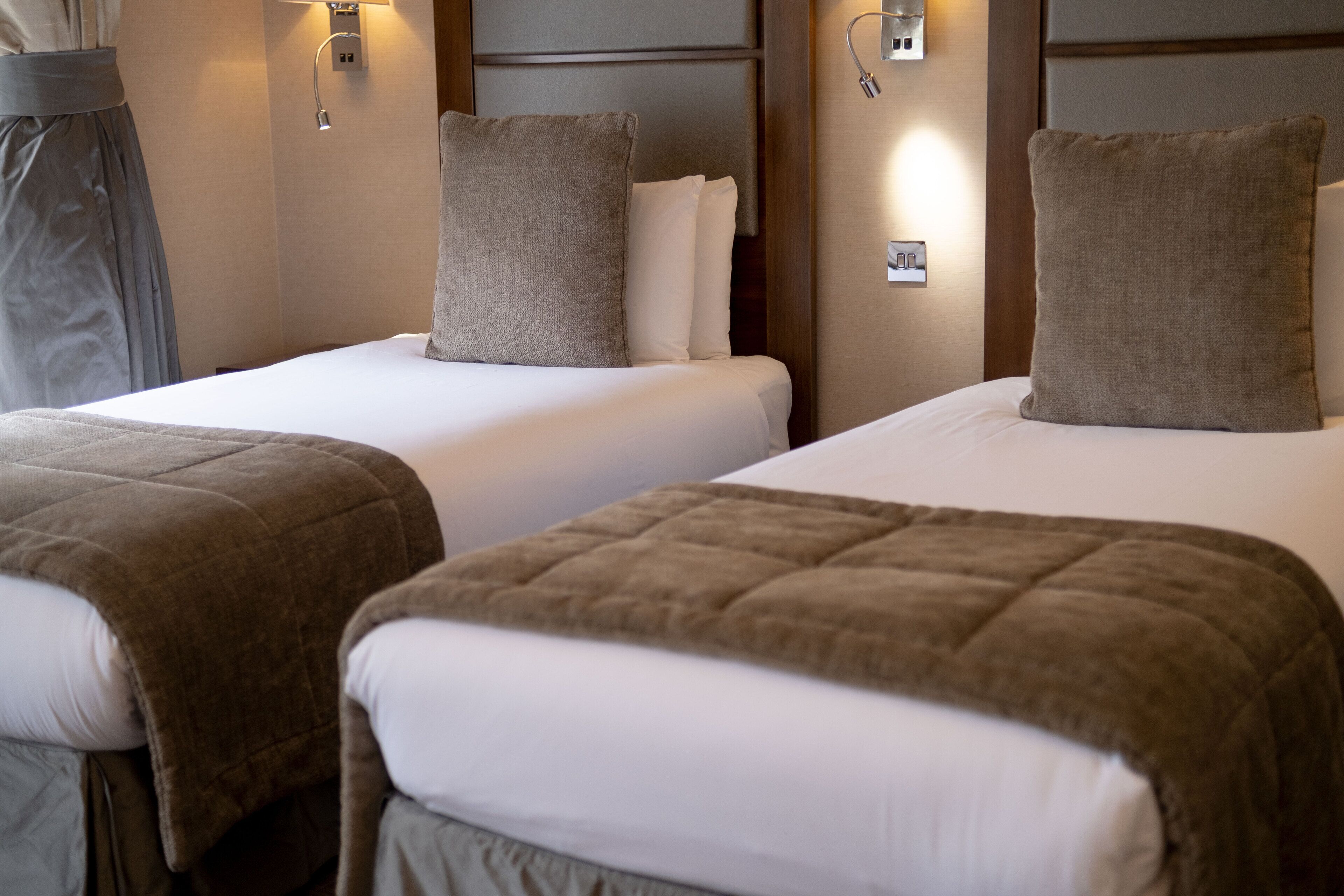 Une chambre d’hôtel avec deux lits, chacun recouvert d’une couverture marron et de draps blancs.