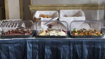A buffet table with three covered food displays, including meats, cheeses, and vegetables.