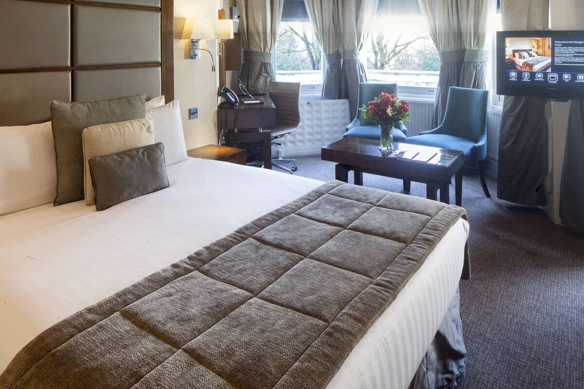 Ein Hotelzimmer mit einem großen Bett, einem Schreibtisch, einem Sessel, einem Fernseher und einem Fenster mit Vorhängen.