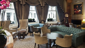 A room with a green upholstered sofa, beige armchairs, a small round table, and a large window with curtains. - Gem Strathmore Hotel (London)