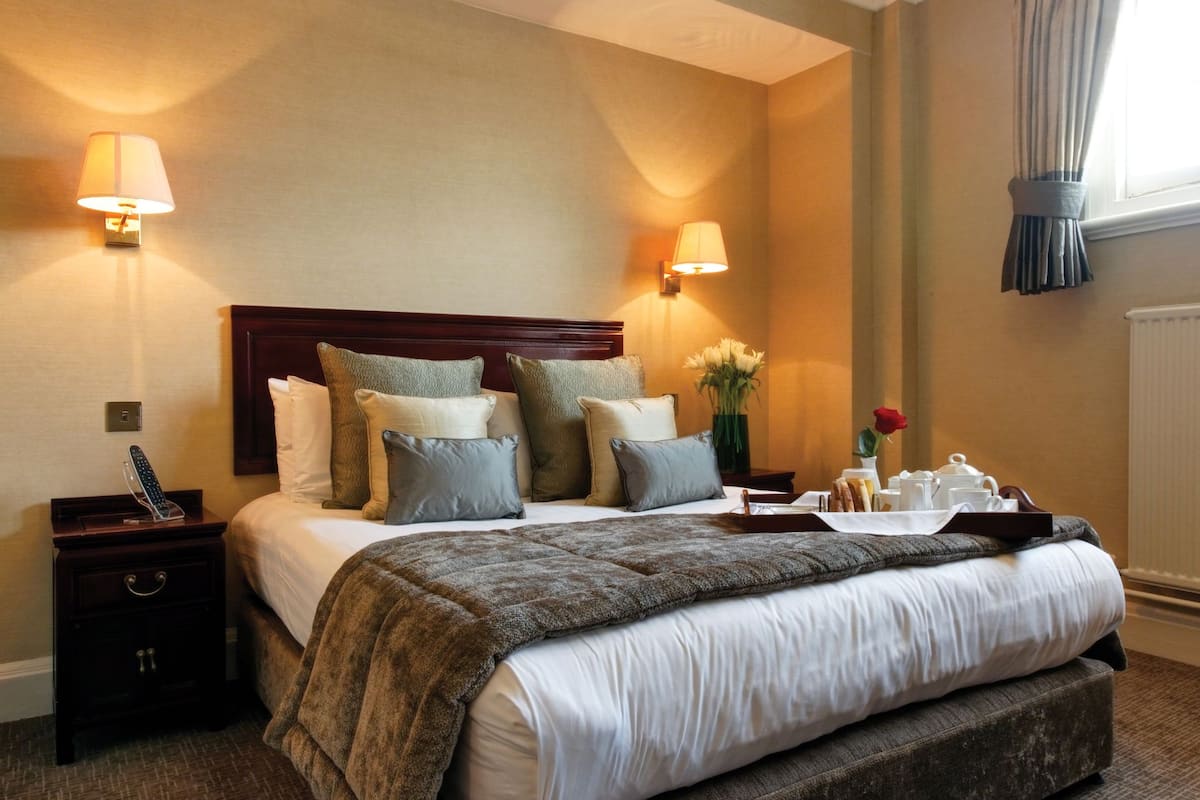 Ein Hotelzimmer mit einem großen Bett, zwei Nachttischen, einer Lampe und einem Fenster mit Vorhängen.