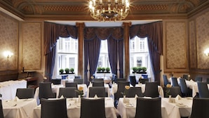 Een stijlvolle eetzaal met gedekte tafels, weelderige kroonluchters en grote ramen met gordijnen.