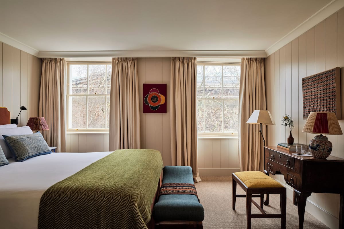Une chambre d’hôtel avec un grand lit, un banc, une commode et une fenêtre avec des rideaux.