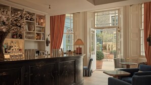 Un espace bar avec un comptoir sombre, des étagères remplies de verres et une vue sur une terrasse extérieure aménagée avec des sièges.