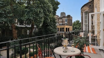 Ein Balkon mit Tisch und Stühlen, umgeben von einem Geländer, mit Gebäuden und Bäumen im Hintergrund.