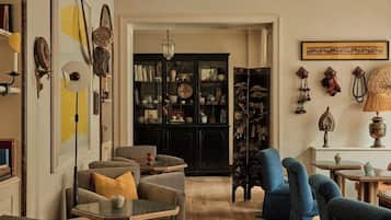 Un salon comprenant un canapé, des fauteuils, une table basse, une bibliothèque et une lampe.
