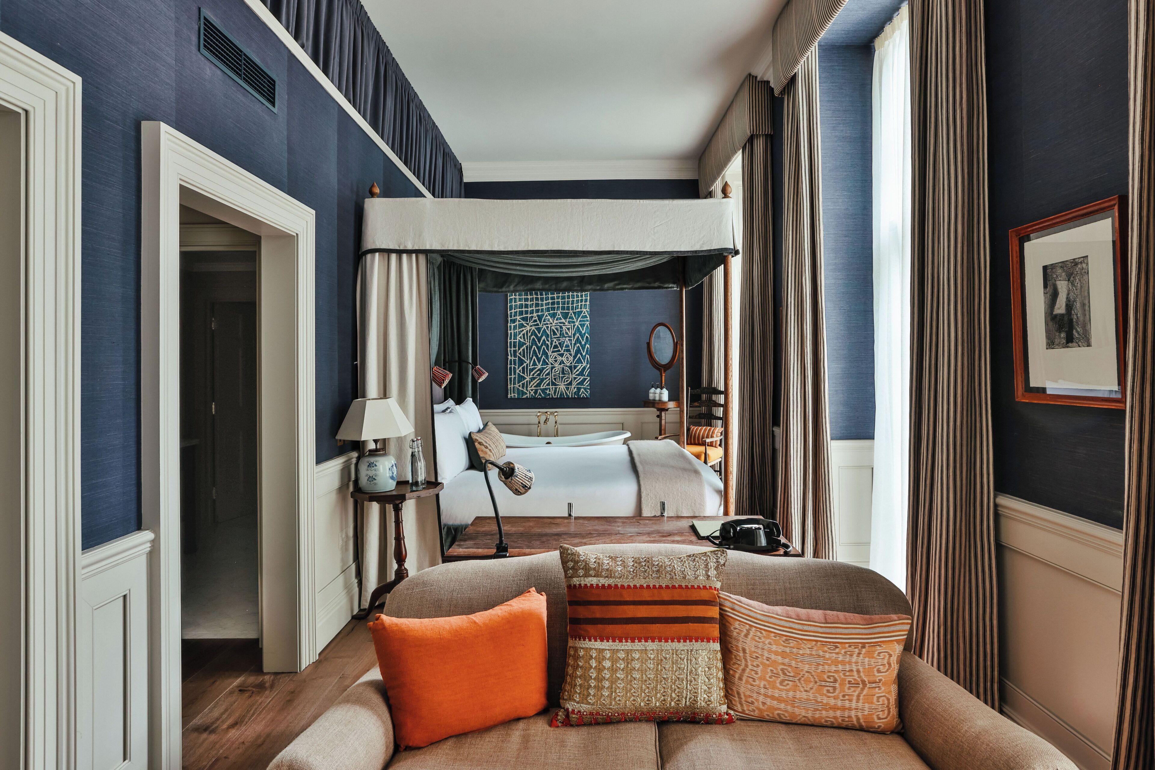 Een hotelkamer met een groot bed, een zithoek met een bank, een spiegel en uitzicht op de badkamer.