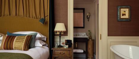 Ein Hotelzimmer mit Bett, Nachttisch, Lampe, Spiegel, Badezimmer mit Badewanne und einem gerahmten Bild an der Wand.