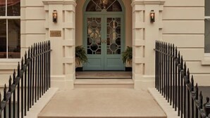 Une entrée d’immeuble avec une porte verte, des colonnes blanches et une grille en fer noir.
