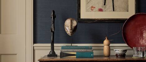 Een houten dressoir met daarboven een ingelijst schilderij, een boek getiteld 'The Fabric of India' en een decoratief masker.
