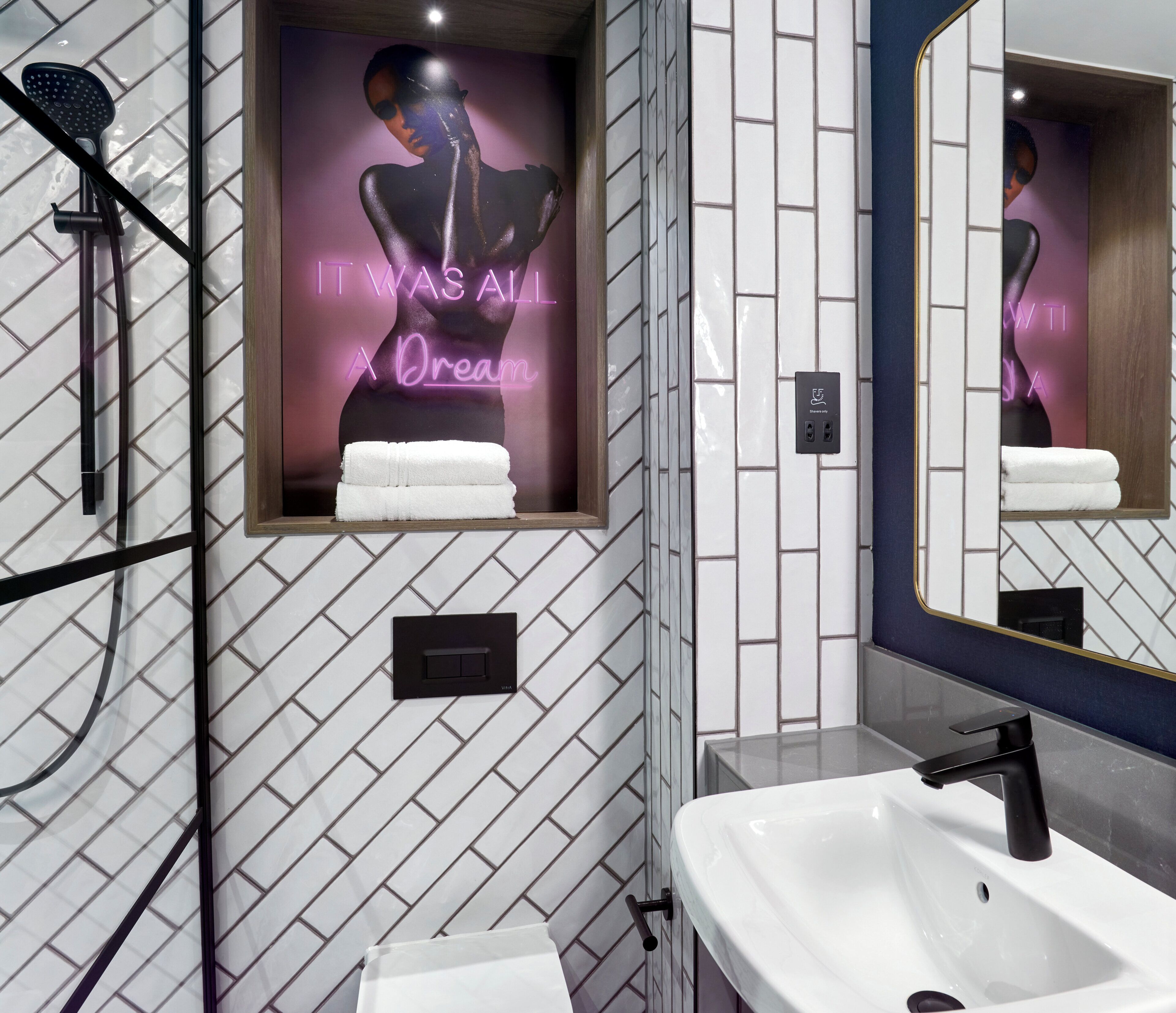 A modern bathroom with a shower, a sink, and a mirror. There is a neon sign on the wall and a towel rack.