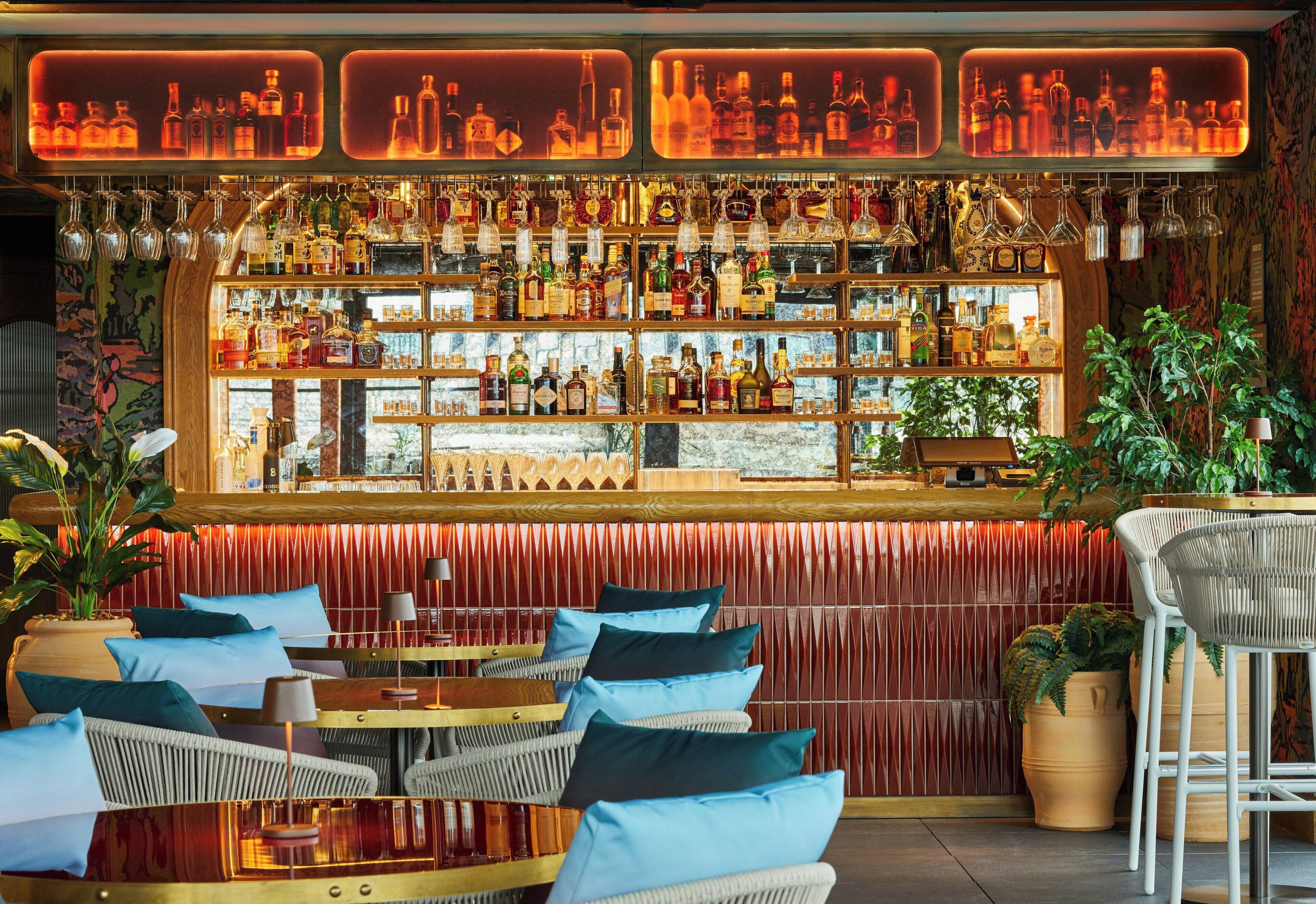 A bar area with multiple shelves of liquor bottles, wicker chairs, and a red textured wall.