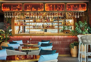 A bar area with multiple shelves of liquor bottles, wicker chairs, and a red textured wall.