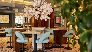 Un área de bar moderna con una mesa central, taburetes de bar y un árbol blanco decorativo.