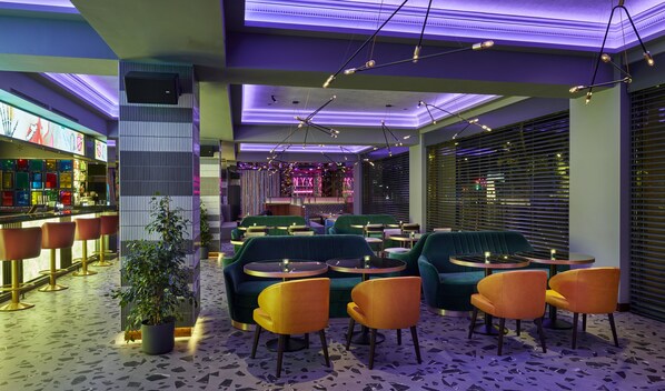 Un interior moderno con zonas de estar, un bar y una barra iluminada con neón.