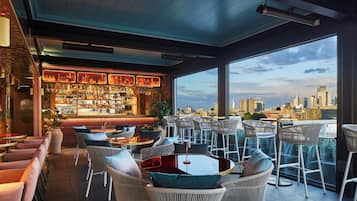 Un bar situé sur le toit, offrant une vue sur la ville, avec des meubles en osier et un comptoir bien garni.
