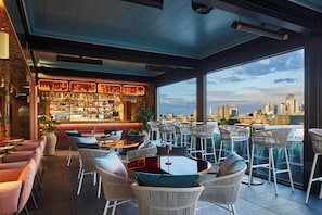 A rooftop bar with a city view, wicker furniture, and a well-stocked bar area.