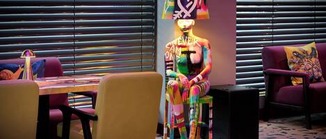 A room with a dining table, chairs, a sofa, and a colorful artwork on the wall.