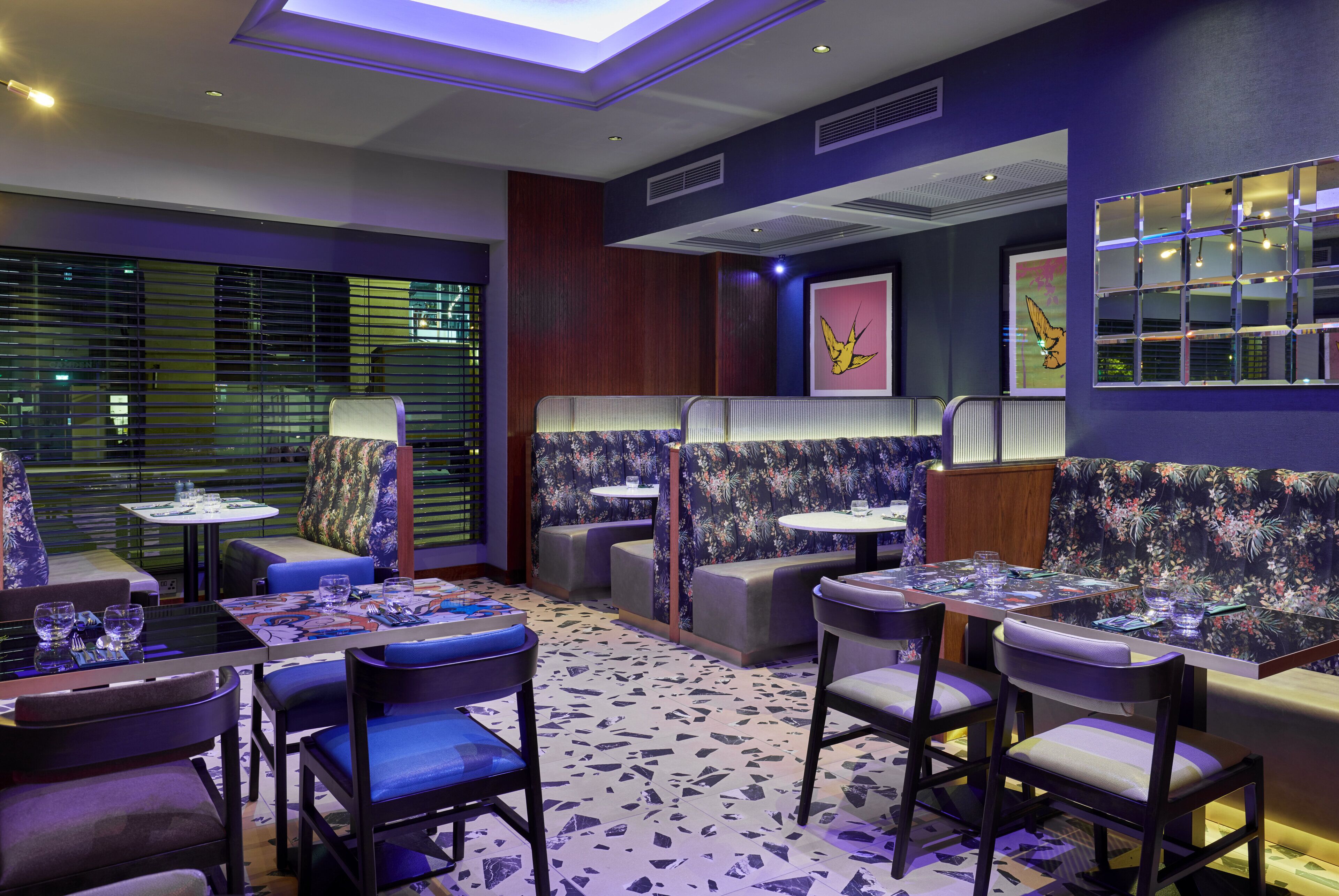 A modern restaurant with booths and tables, featuring a terrazzo floor and purple walls.