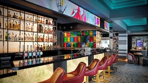 Zona de bar con distintas opciones de asientos, una variedad de botellas en estanterías y un mural colorido en la pared.