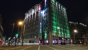 Un hotel de varios pisos con un llamativo letrero de 'NYX', amplias ventanas y un diseño arquitectónico moderno.