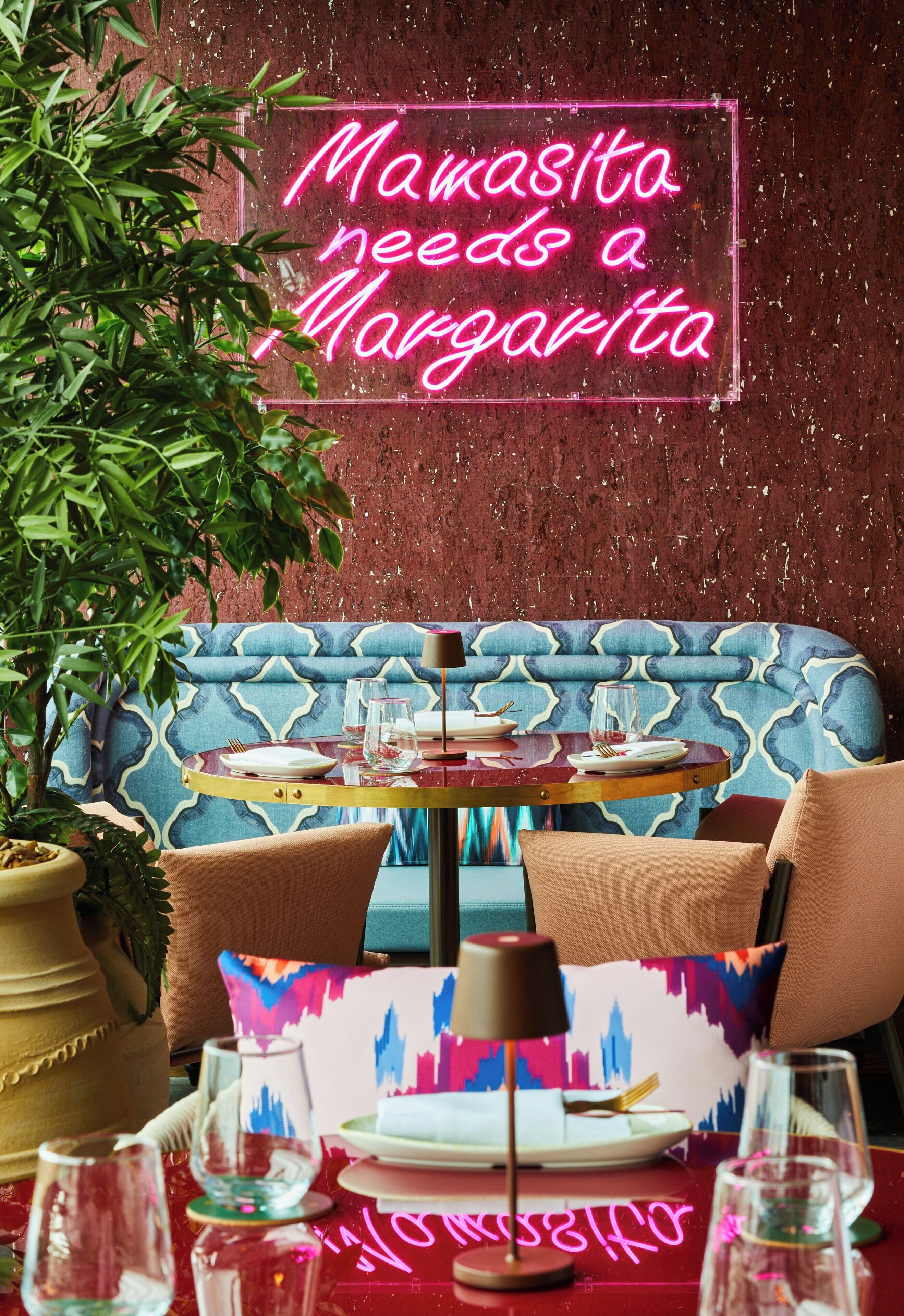 Interior de restaurante con un letrero de neón, un sofá azul estampado y una mesa lista para comer.