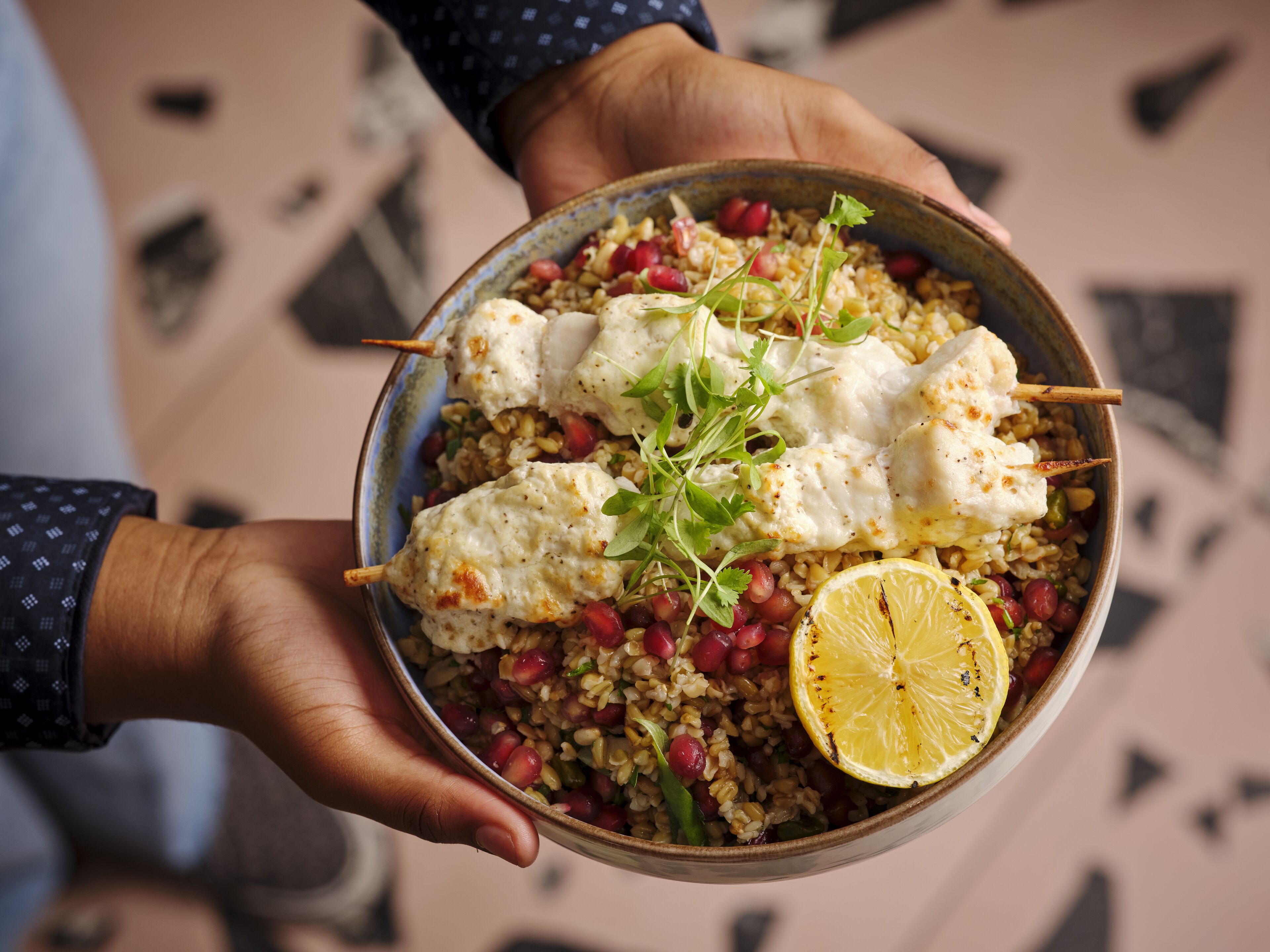 A bowl of food with grilled chicken, pomegranate seeds, and a lemon slice.