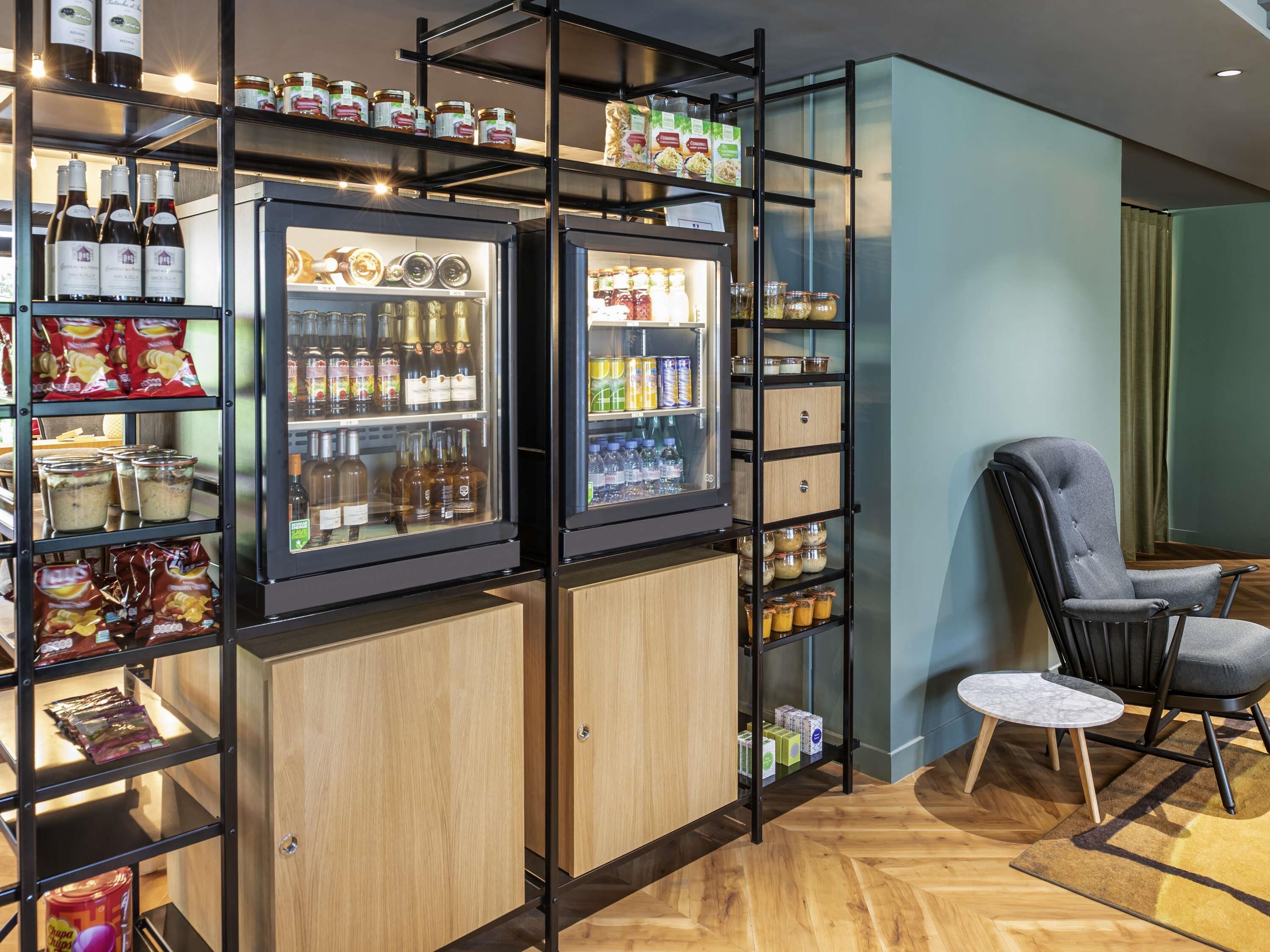 Een hotelkamer met een minibar, plankjes met snacks, een stoel en een kleine tafel.