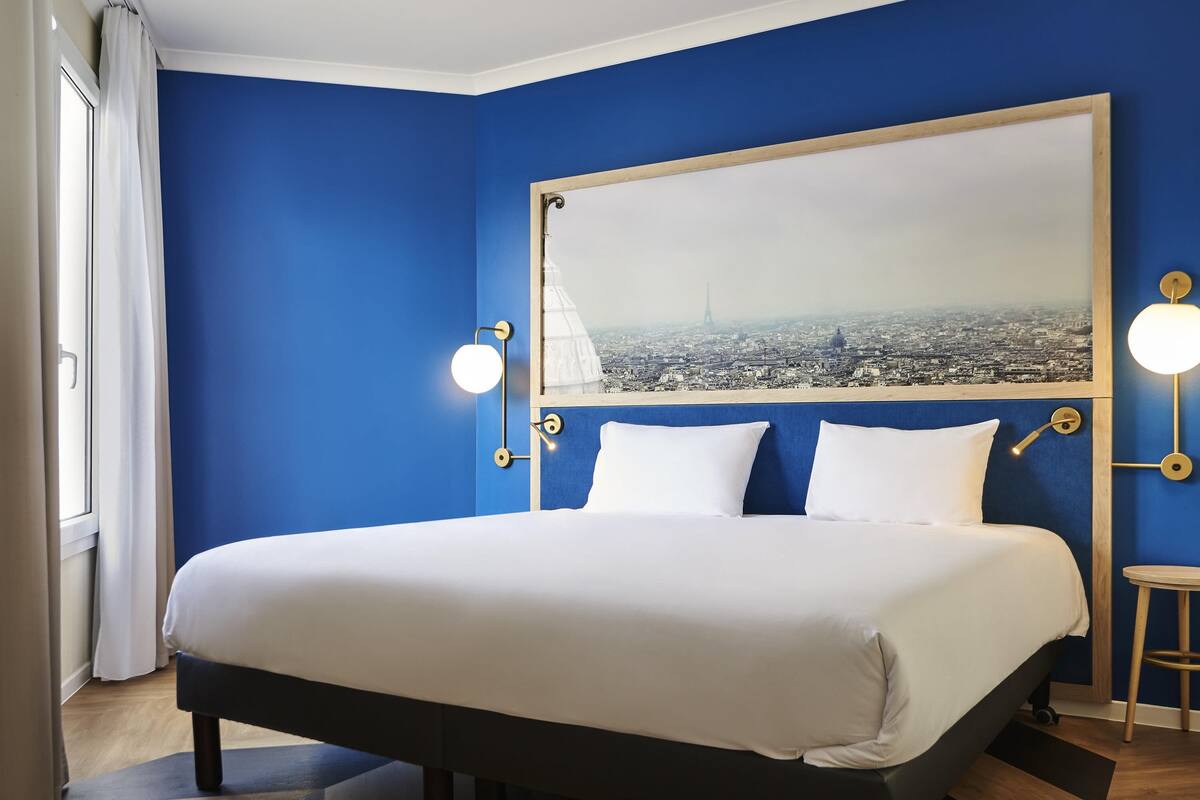 Camera d'albergo con un letto grande, vista sulla città e una parete blu.