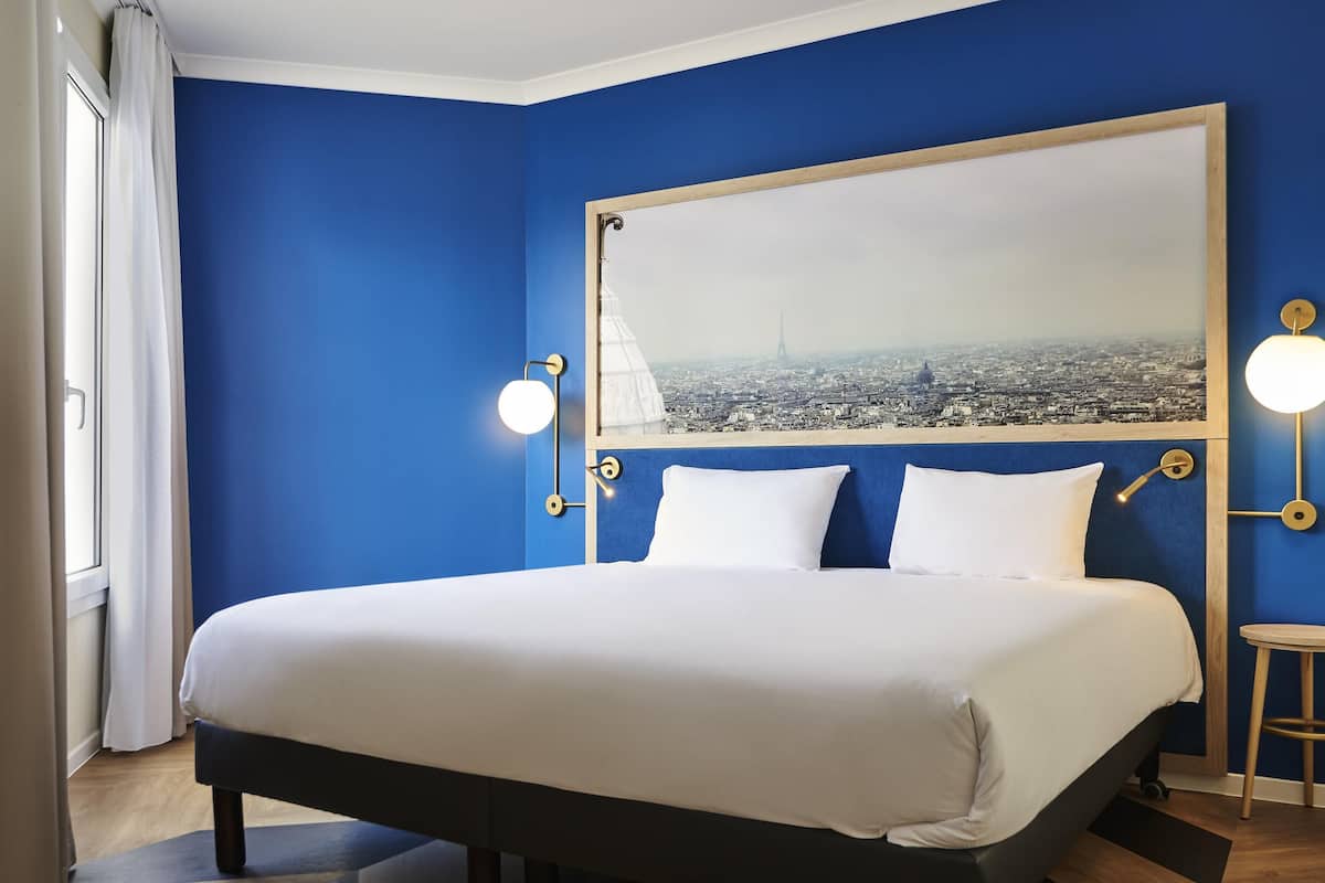 Ein Hotelzimmer mit einem großen Bett, Blick auf die Stadt und einer blauen Wand.