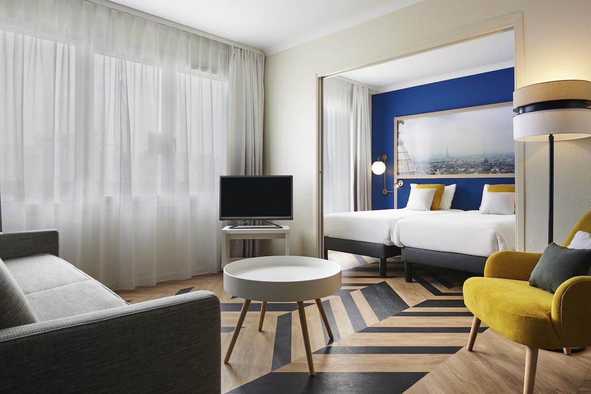 Habitación de hotel con cama, televisión, una mesa redonda, sofá y una silla.