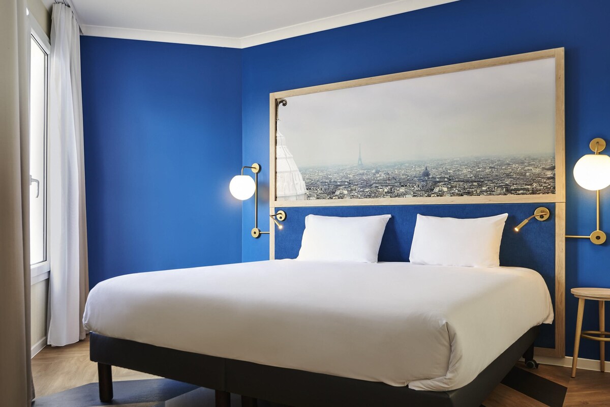 Une chambre d’hôtel avec un grand lit, une vue sur la ville et un mur bleu.