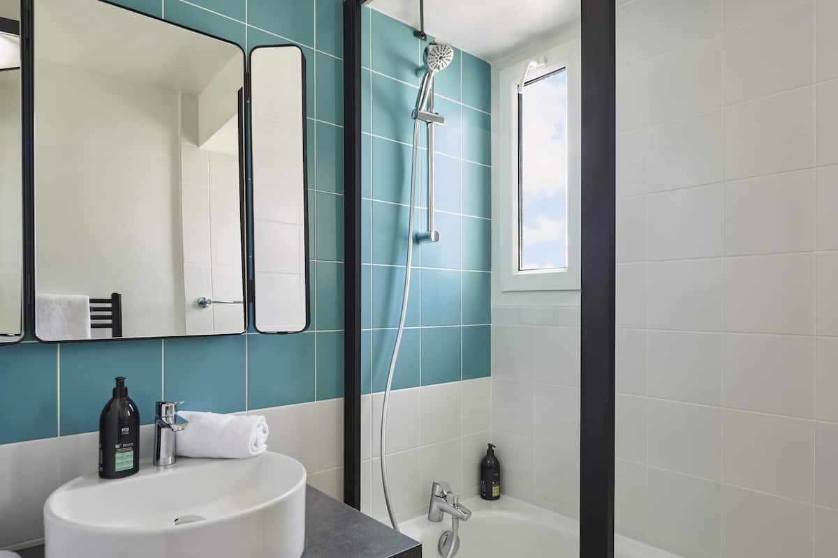 A bathroom with a white sink, a mirror, a shower, and a window.