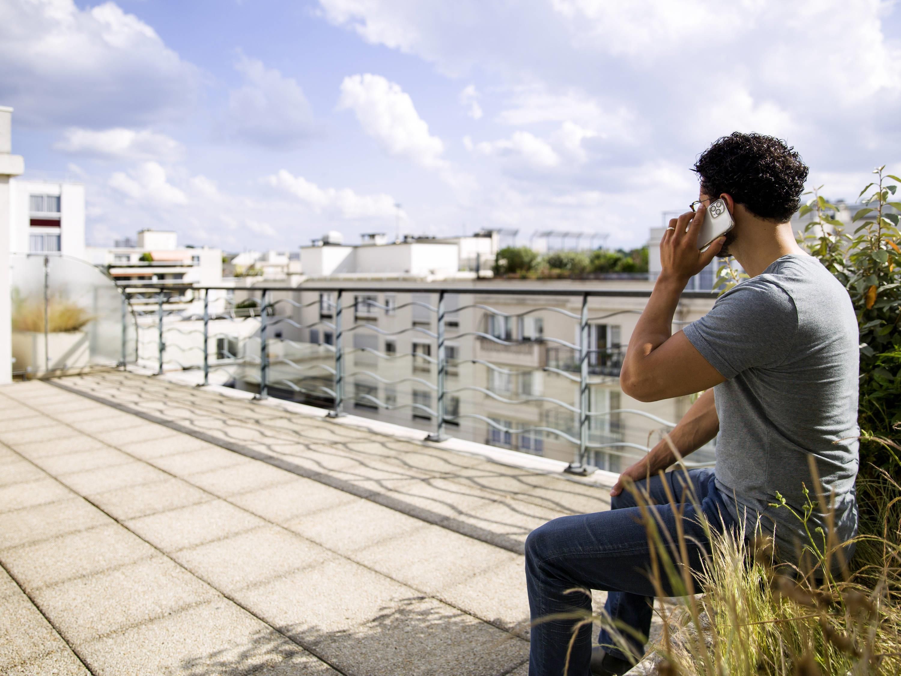 A person sitting on a balcony with a view of buildings and a clear sky.