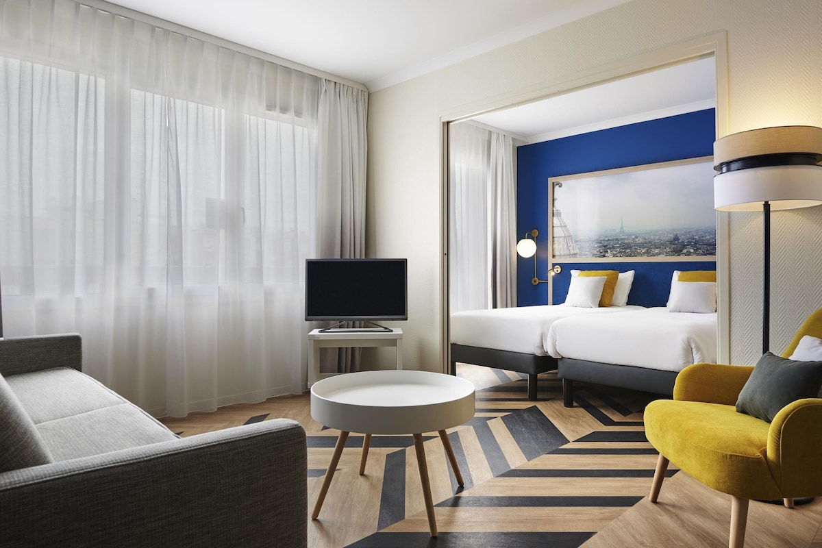 Een hotelkamer met een bed, een televisie, een ronde tafel, een bank en een stoel.