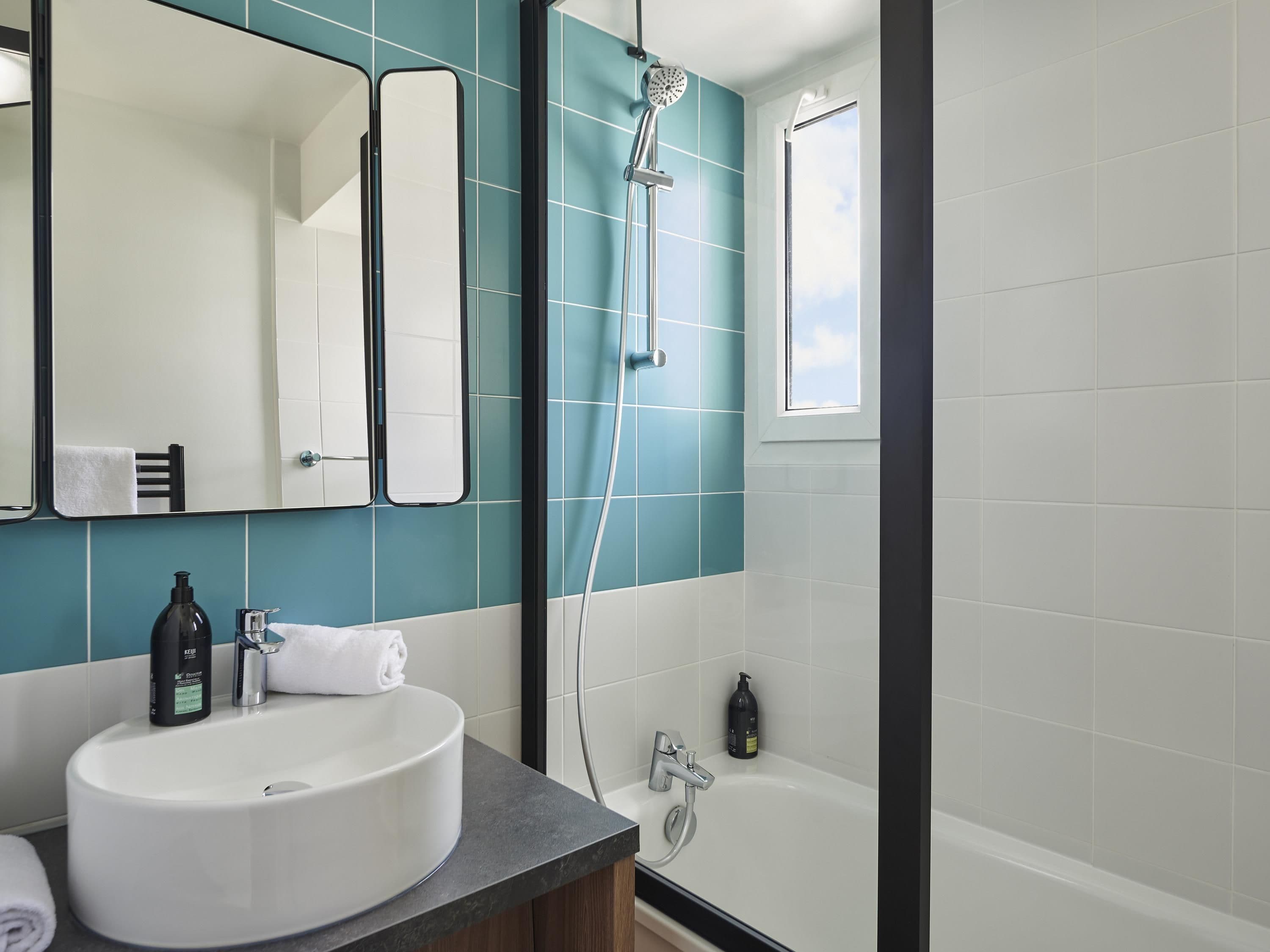 A bathroom with a white sink, a mirror, a shower, and a window.