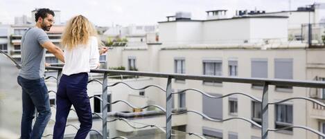 A couple standing on a balcony with a view of other buildings.