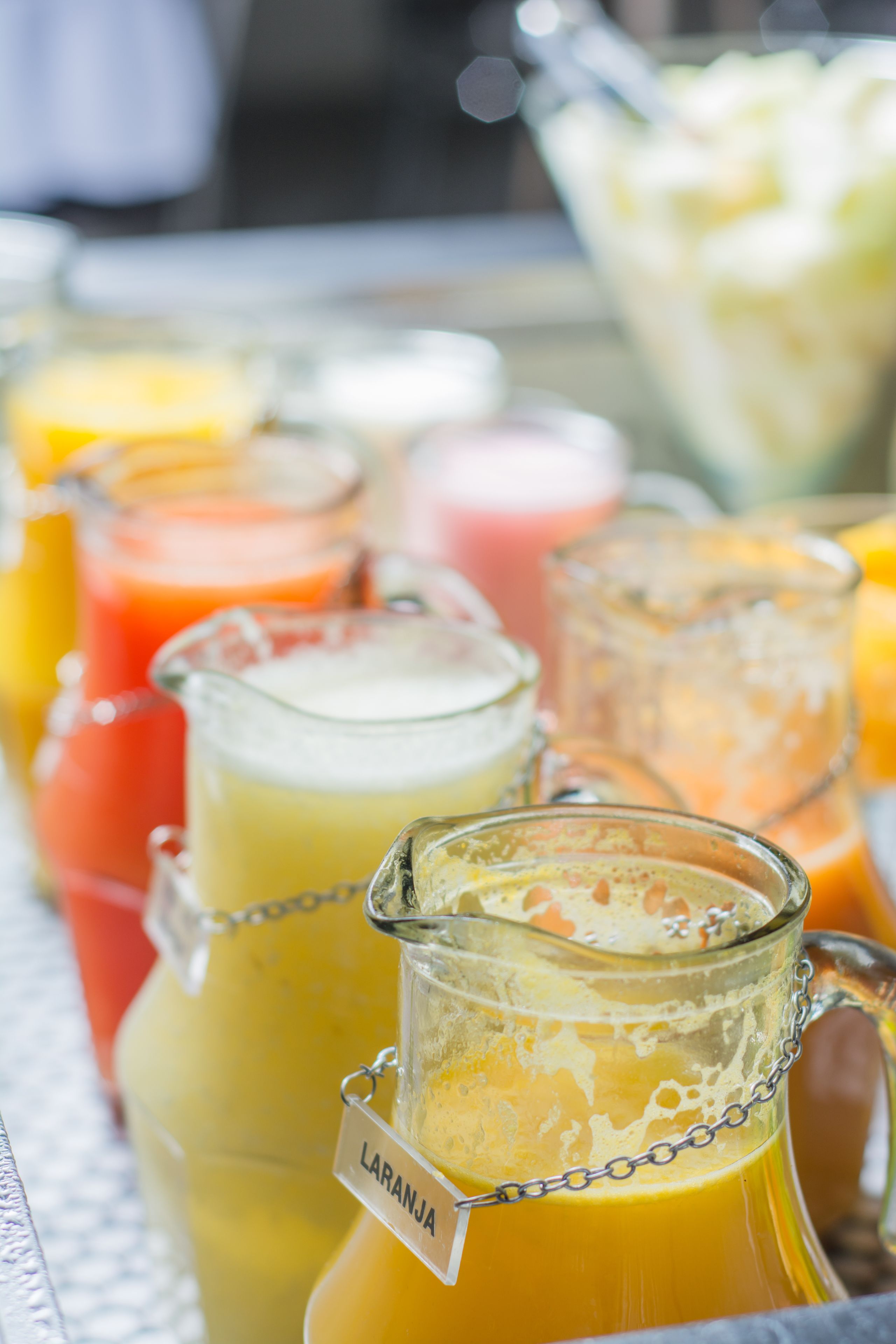 A variety of colorful beverages in glass containers, including a pitcher labeled "LARANJA".