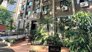 A multi-story building with air conditioning units on the exterior, surrounded by lush greenery and a paved walkway.
