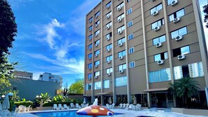 A swimming pool with a mushroom-shaped water feature, surrounded by lounge chairs and a tall building with multiple windows and air conditioning units.
