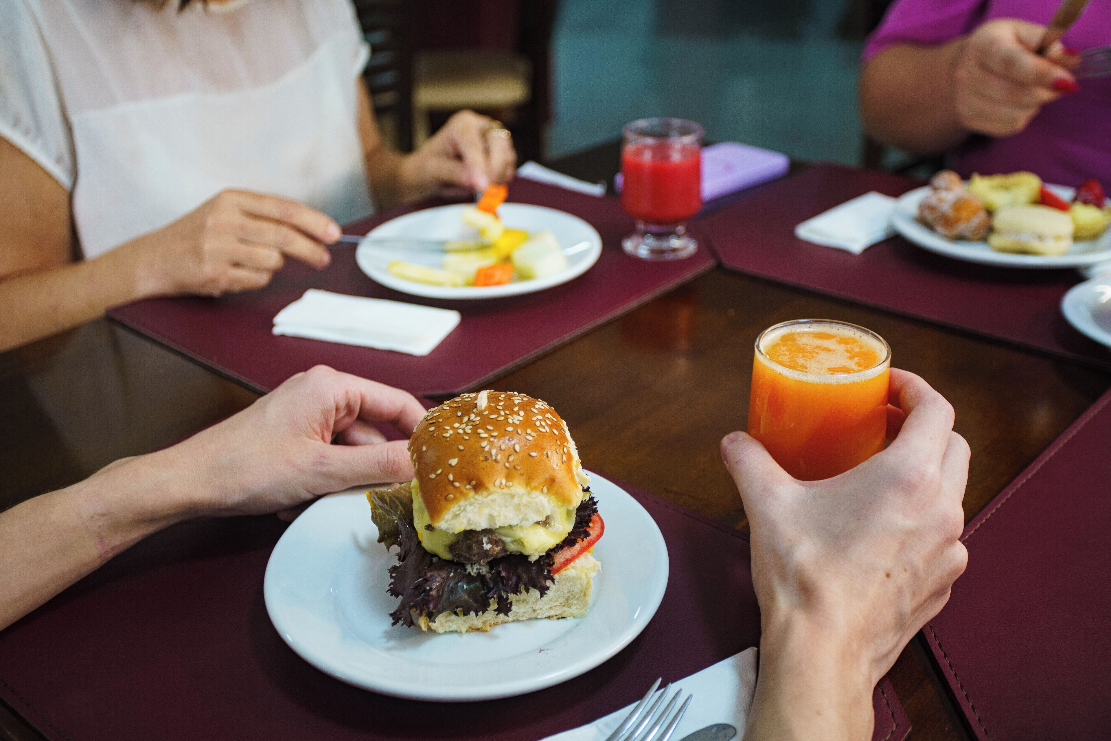 Una mesa de comedor con una comida que incluye una hamburguesa, un vaso de jugo de naranja y un plato de fruta.
